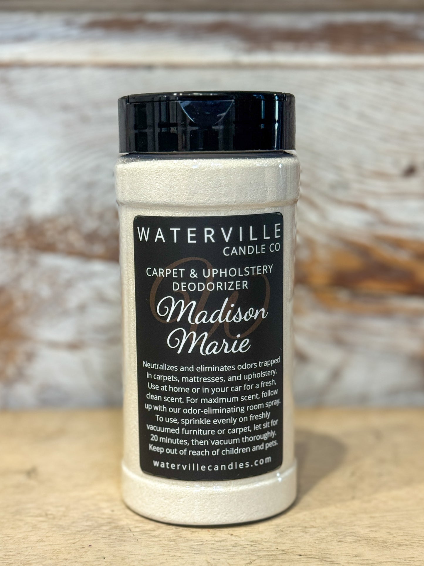 Jar of Waterville Candle Co. carpet and upholstery deodorizer on a wooden surface with a blurred background.