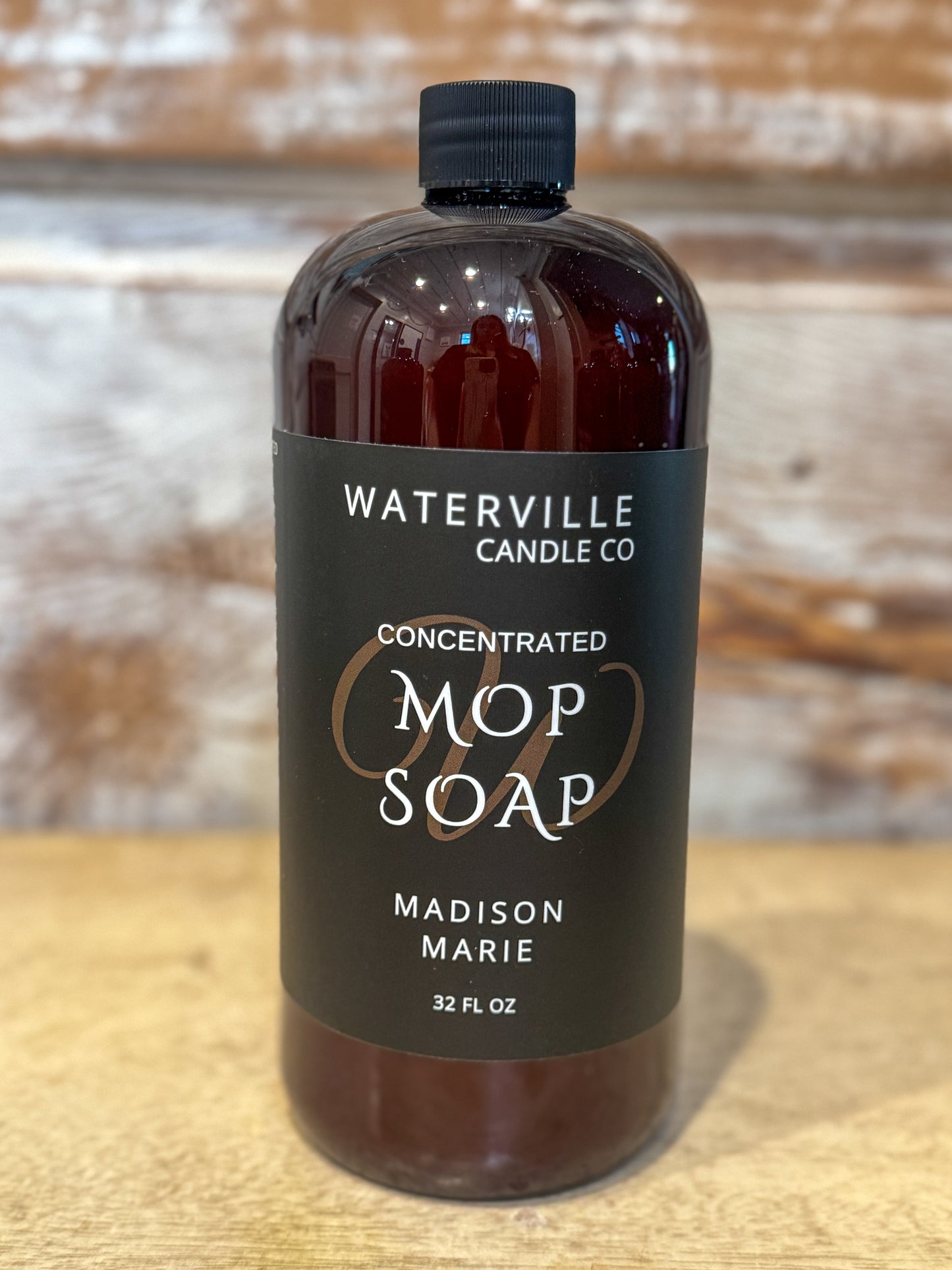 Bottle of Waterville Candle Co. Mop Soap on a wooden surface with a blurred background