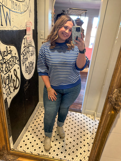 Woman taking a mirror selfie wearing a blue and white striped shirt and jeans in a room with a decorative wall.