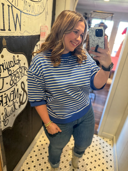 Woman taking a mirror selfie wearing a blue and white striped sweater and jeans.