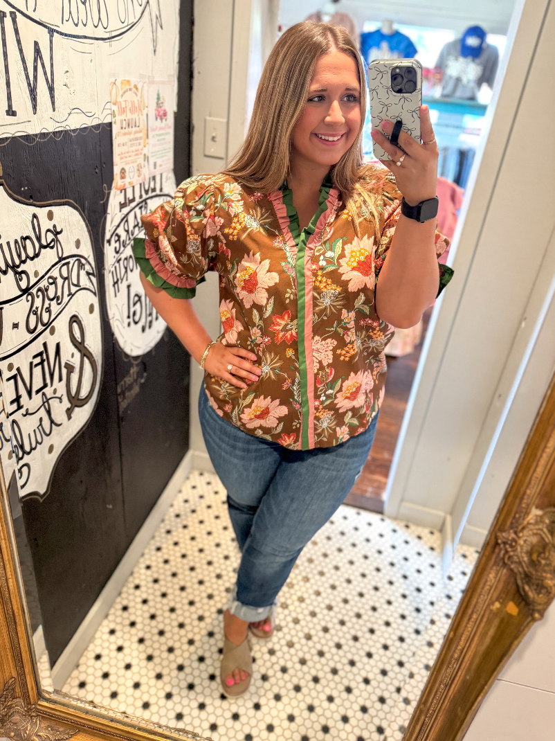 Woman taking a mirror selfie wearing a floral blouse and jeans in a store.
