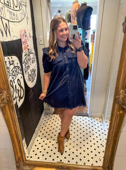 Woman taking a mirror selfie wearing a navy blue dress in a store.