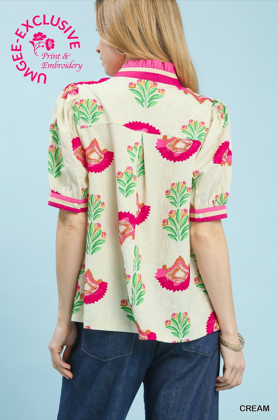Woman wearing a cream blouse with pink and green floral patterns on a light blue background.