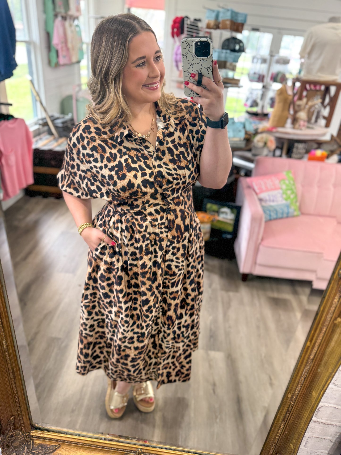 Woman taking a mirror selfie wearing a leopard print dress in a store.