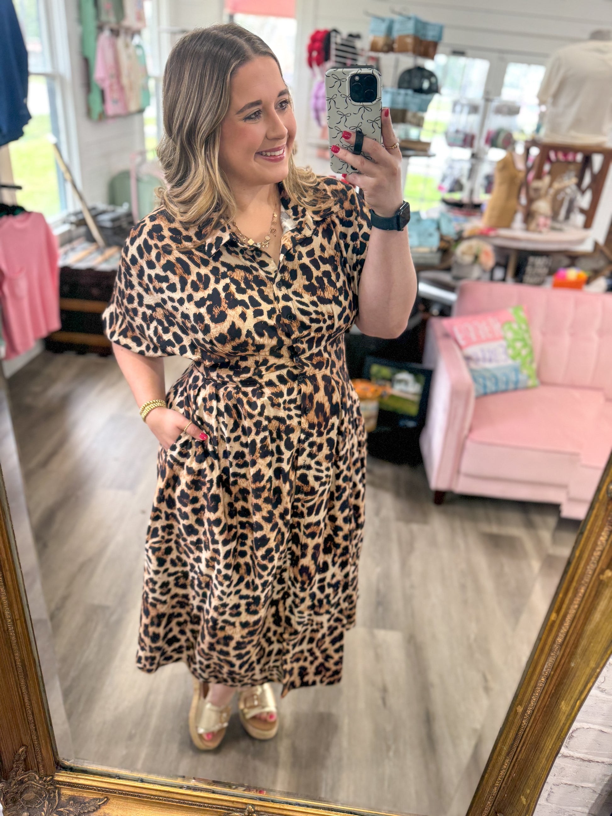 Woman taking a mirror selfie wearing a leopard print dress in a store.
