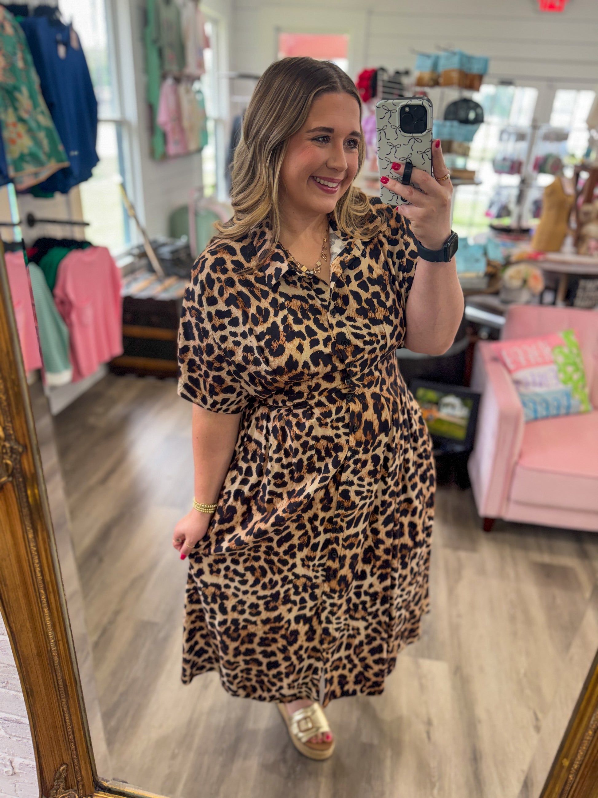 Woman wearing a leopard print dress taking a mirror selfie in a store.