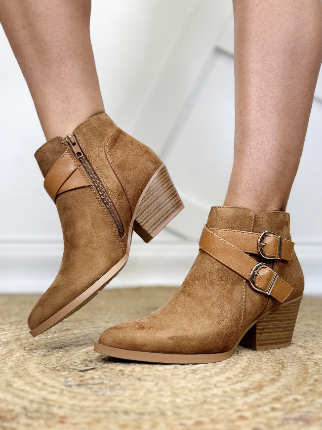 Brown ankle boots with straps worn by a person on a neutral background