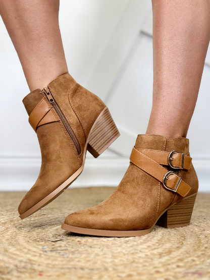 Brown ankle boots with straps worn by a person on a neutral background