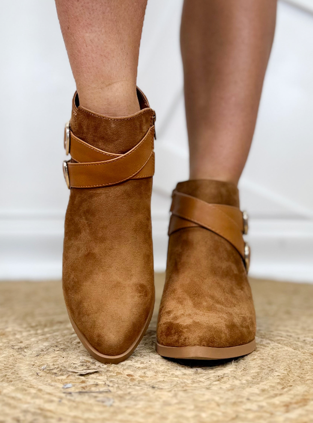 Brown suede ankle boots with strap details on a neutral background