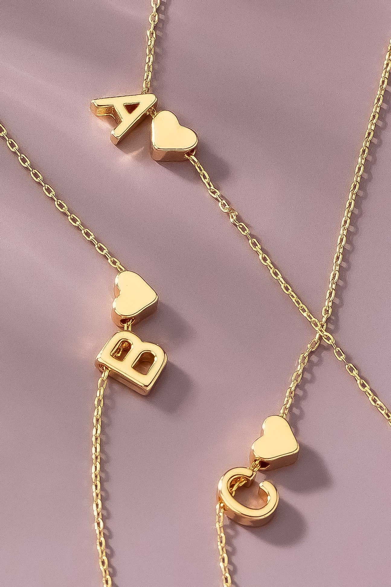 Gold necklaces with letter and heart pendants on a pink background