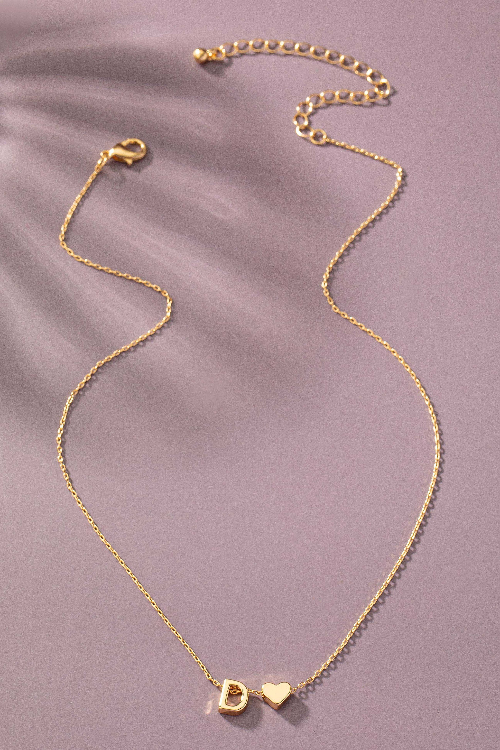 Gold necklace with heart and round pendant on a purple background