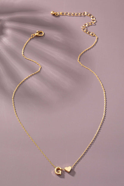 Gold necklace with 'G' and heart pendant on a soft purple background