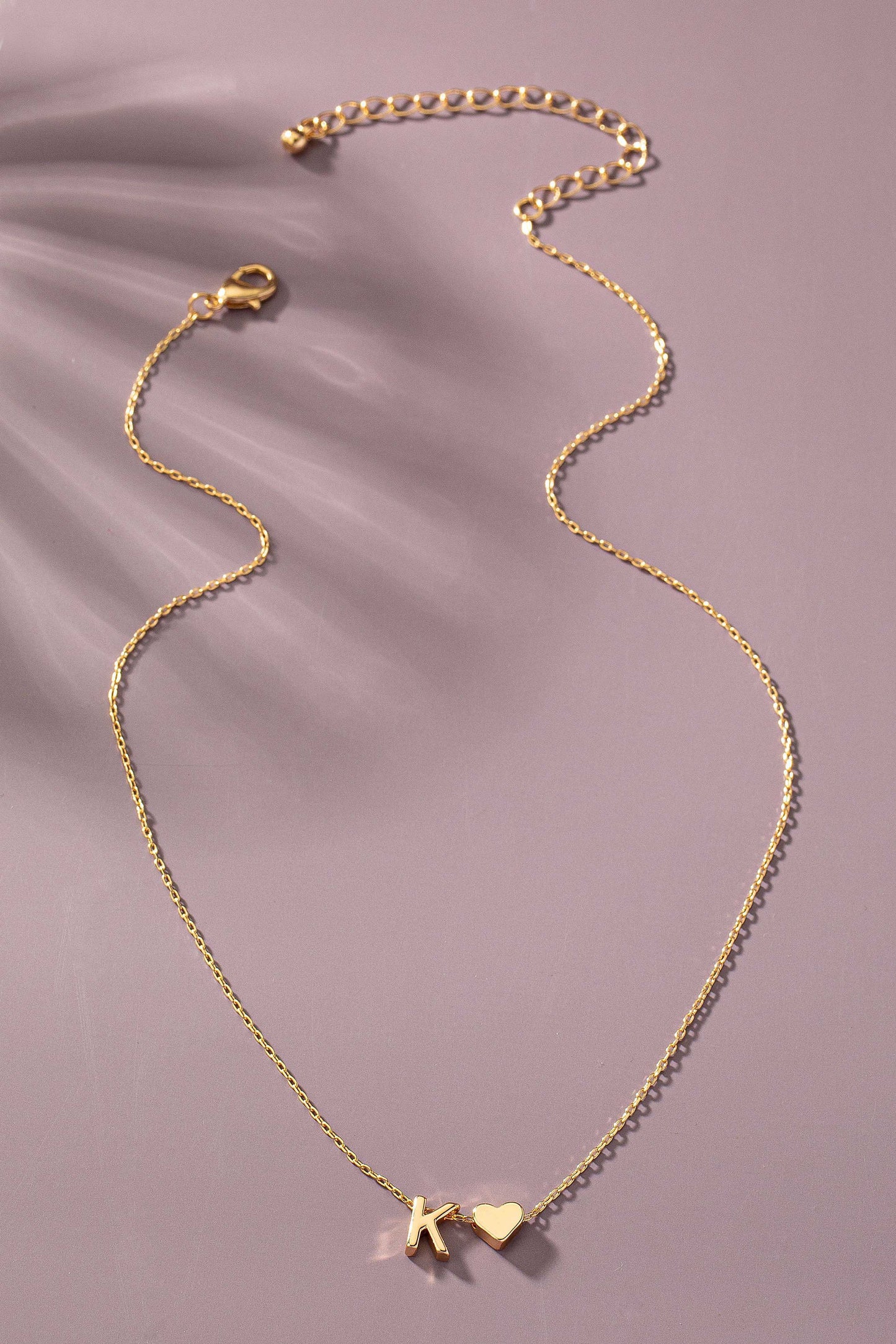 Gold necklace with heart and star charms on a soft pink background