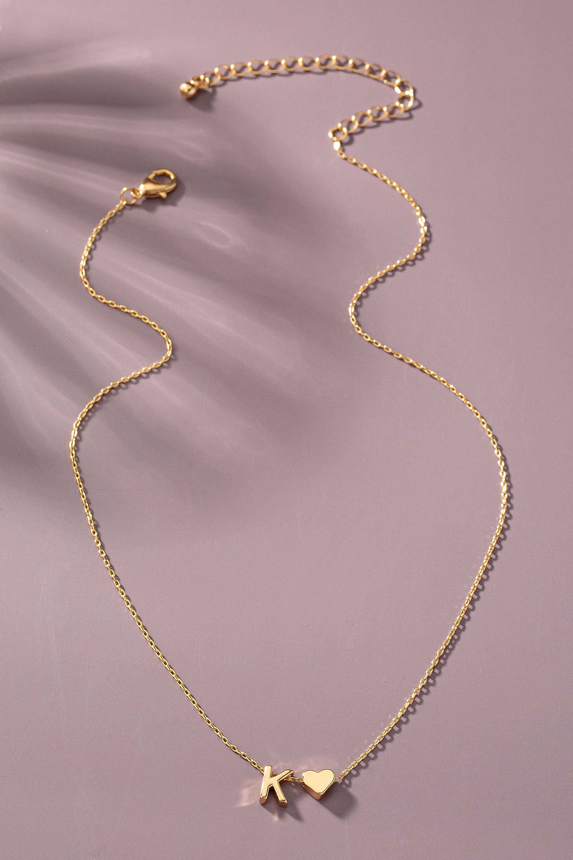 Gold necklace with heart and star charms on a soft pink background