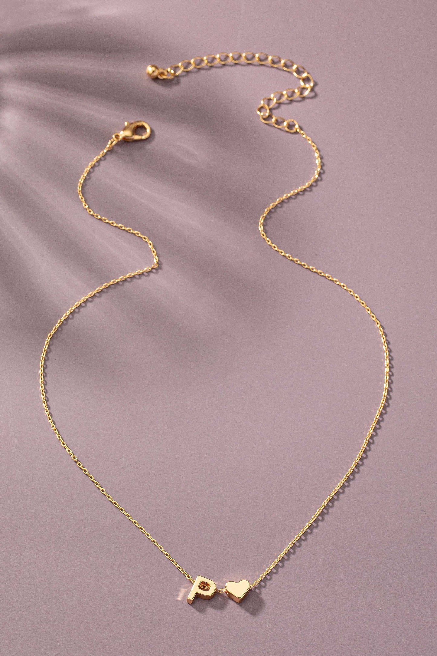 Gold necklace with a heart and 'P' charm on a soft purple background