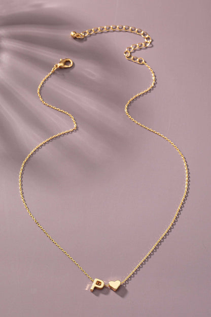 Gold necklace with a heart and 'P' charm on a soft purple background
