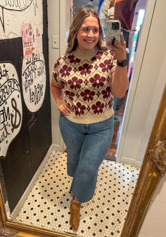 Woman taking a mirror selfie wearing a floral sweater and jeans in a room with a decorative mirror.