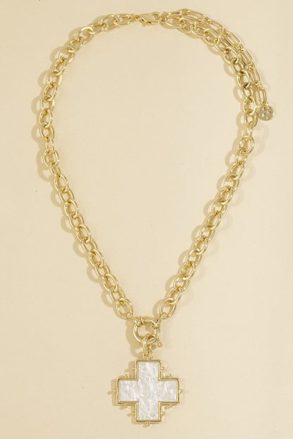 A gold chain necklace with a cross-shaped pendant featuring a white mother-of-pearl center and gold trim, displayed on a solid light beige background.
