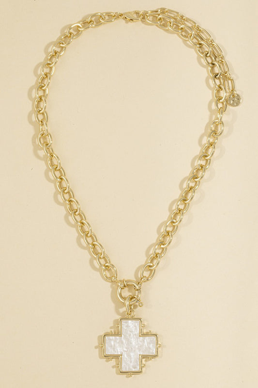 A gold chain necklace with a cross-shaped pendant featuring a white mother-of-pearl center and gold trim, displayed on a solid light beige background.