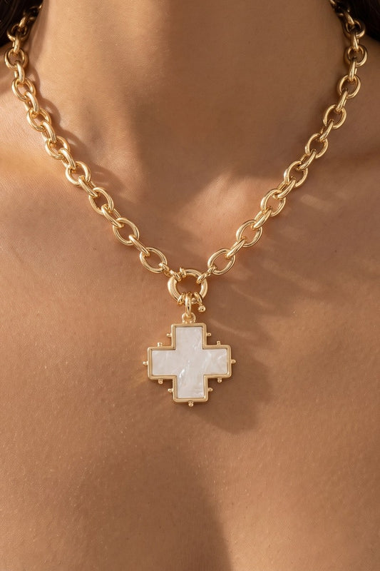 A gold chain necklace with a pixelated cross pendant featuring a white inlay, shown worn on a model's neck.