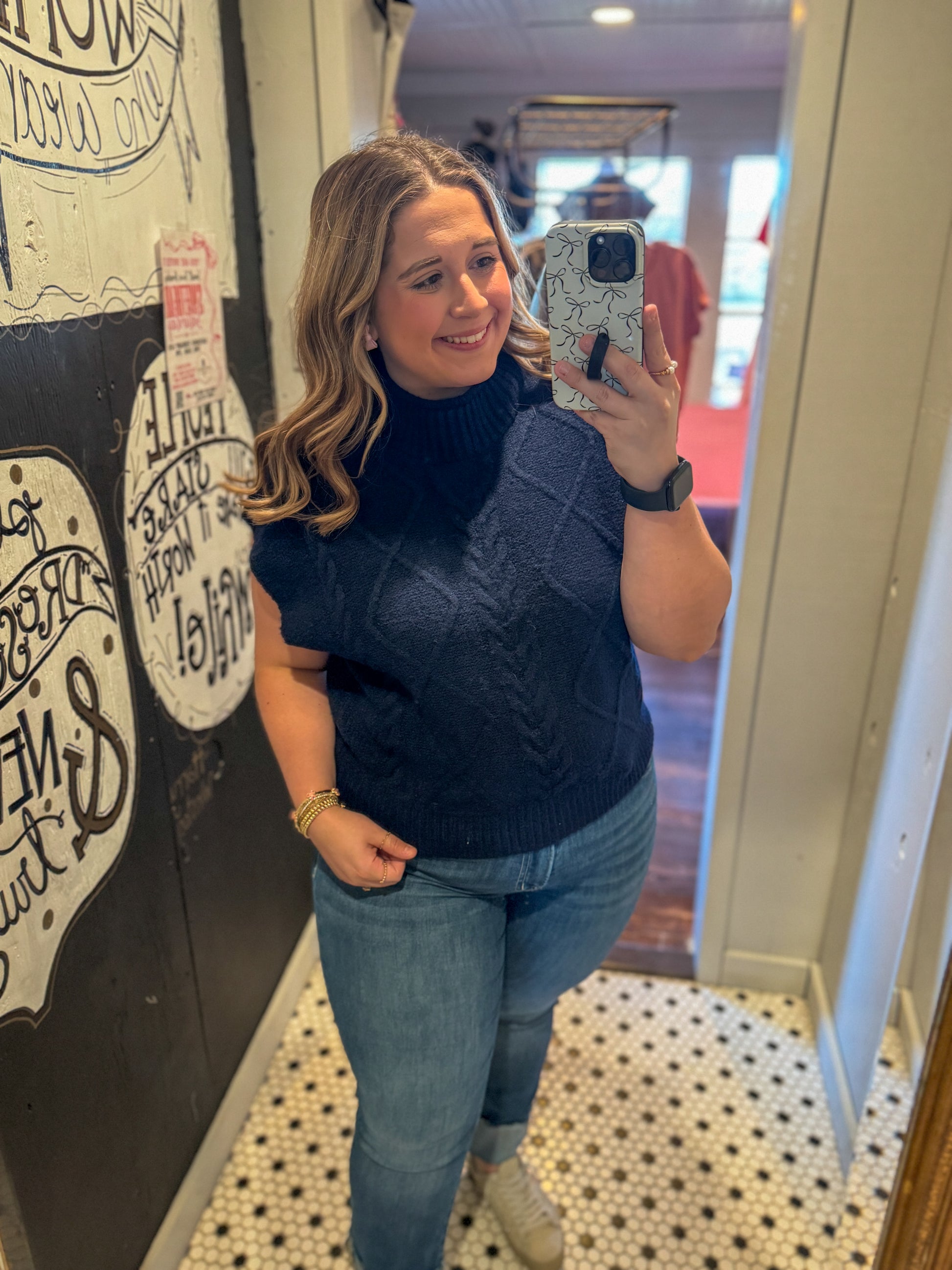Woman taking a mirror selfie wearing a navy blue top and jeans in a store.