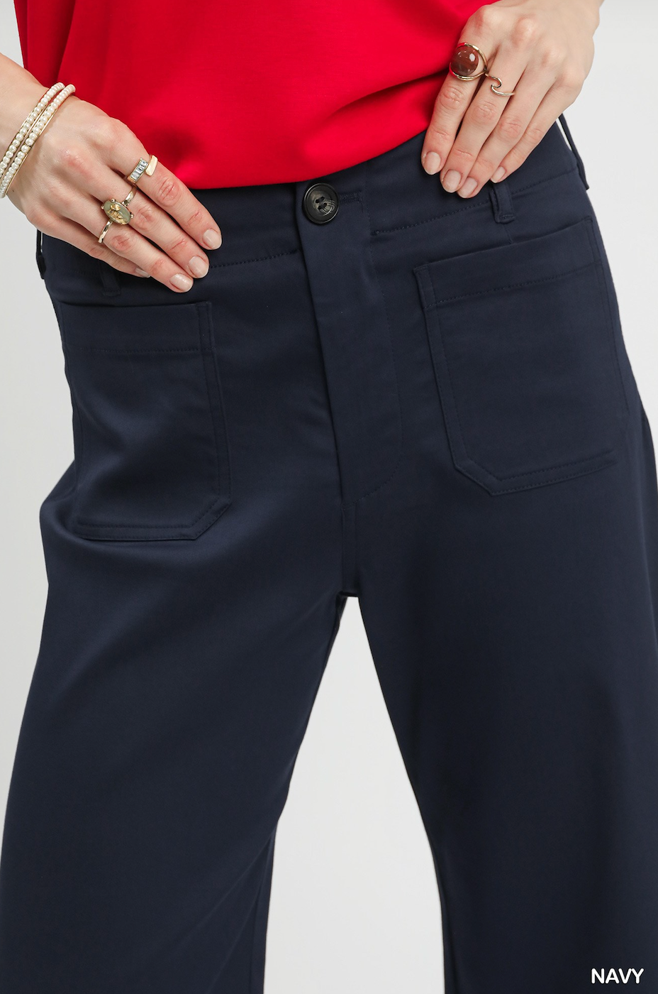 Close-up of a model wearing navy blue wide-leg trousers, styled with a bright red top and gold jewelry, against a light gray background.
