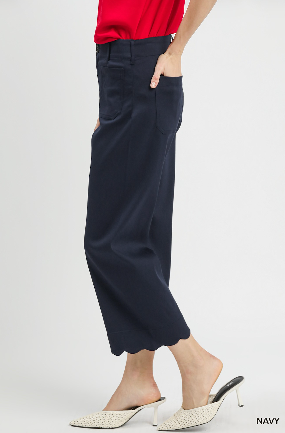 A model wearing navy blue cropped wide-leg trousers with scalloped hems, paired with a red top and white mule heels, shown from the waist down against a light gray studio background.