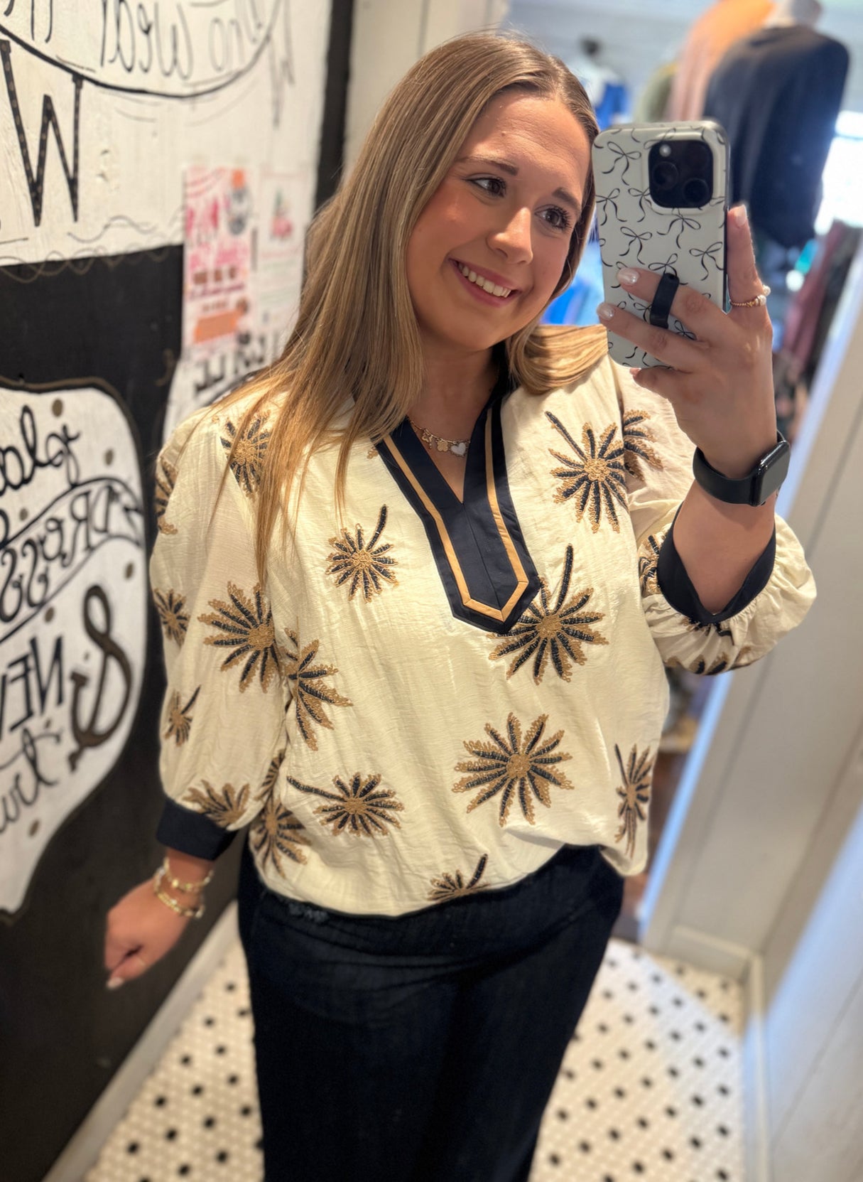 Woman taking a mirror selfie wearing a patterned blouse in a casual setting.