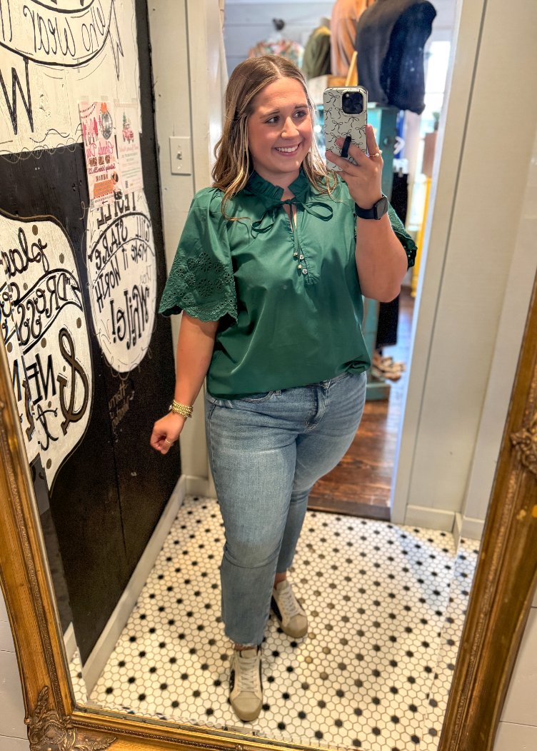Woman taking a mirror selfie wearing a green shirt and blue jeans in a store.