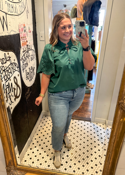 Woman taking a mirror selfie wearing a green shirt and blue jeans in a store.