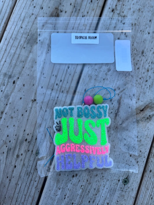 Neon-colored patch with text 'Not bossy just aggressively helpful' on a clear plastic card.