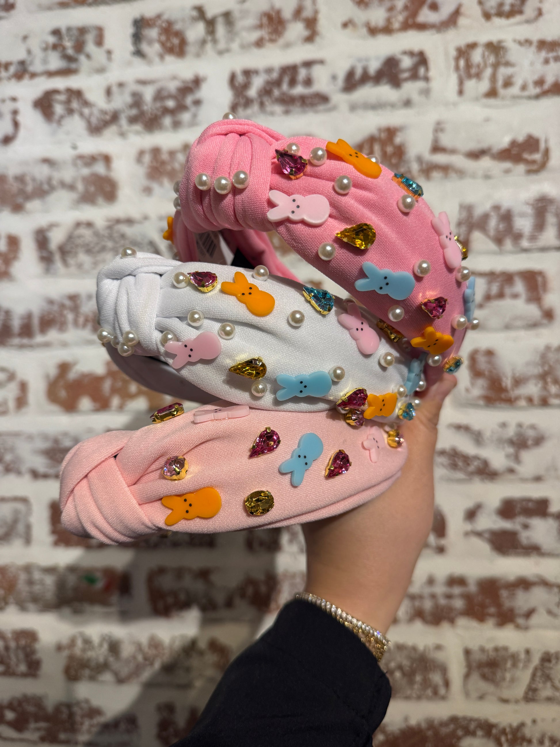 Pair of pink sandals with decorative elements held against a textured wall.