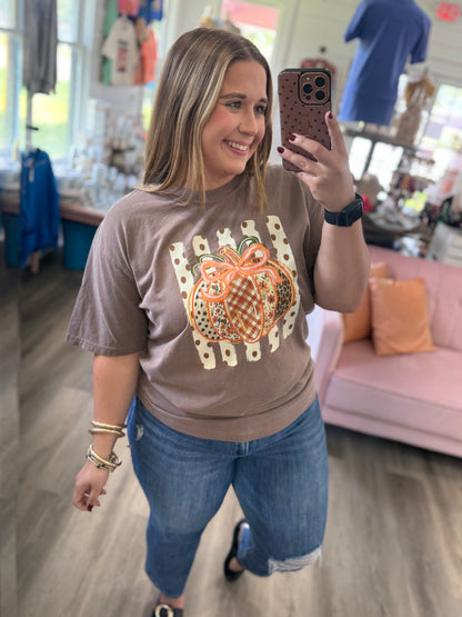 A woman taking a mirror selfie in a boutique, wearing a taupe brown t-shirt with a pumpkin graphic and blue jeans.