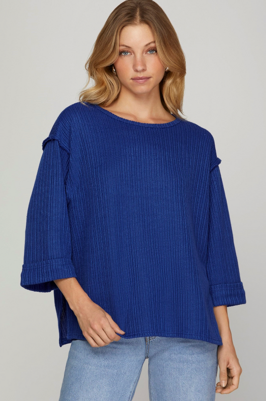 Woman wearing a blue ribbed sweater with ruffled sleeves on a plain background