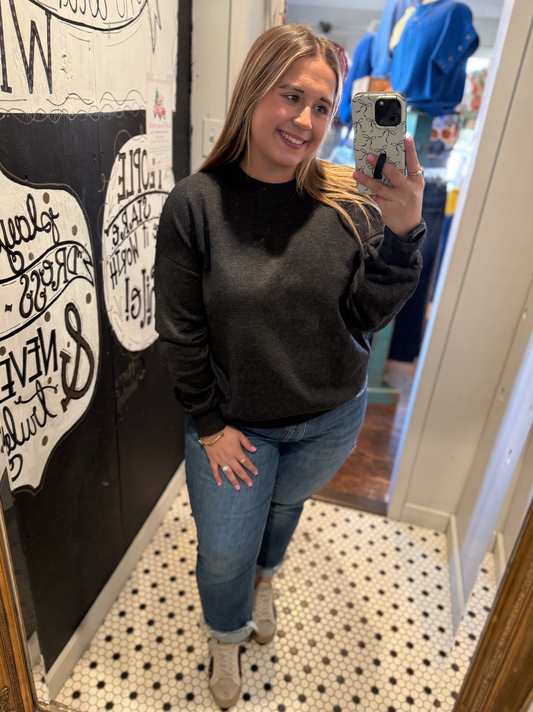 Woman taking a mirror selfie wearing a dark gray sweatshirt and blue jeans in a store.