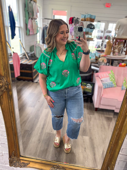 Woman taking a mirror selfie wearing a green floral blouse and blue jeans in a store.