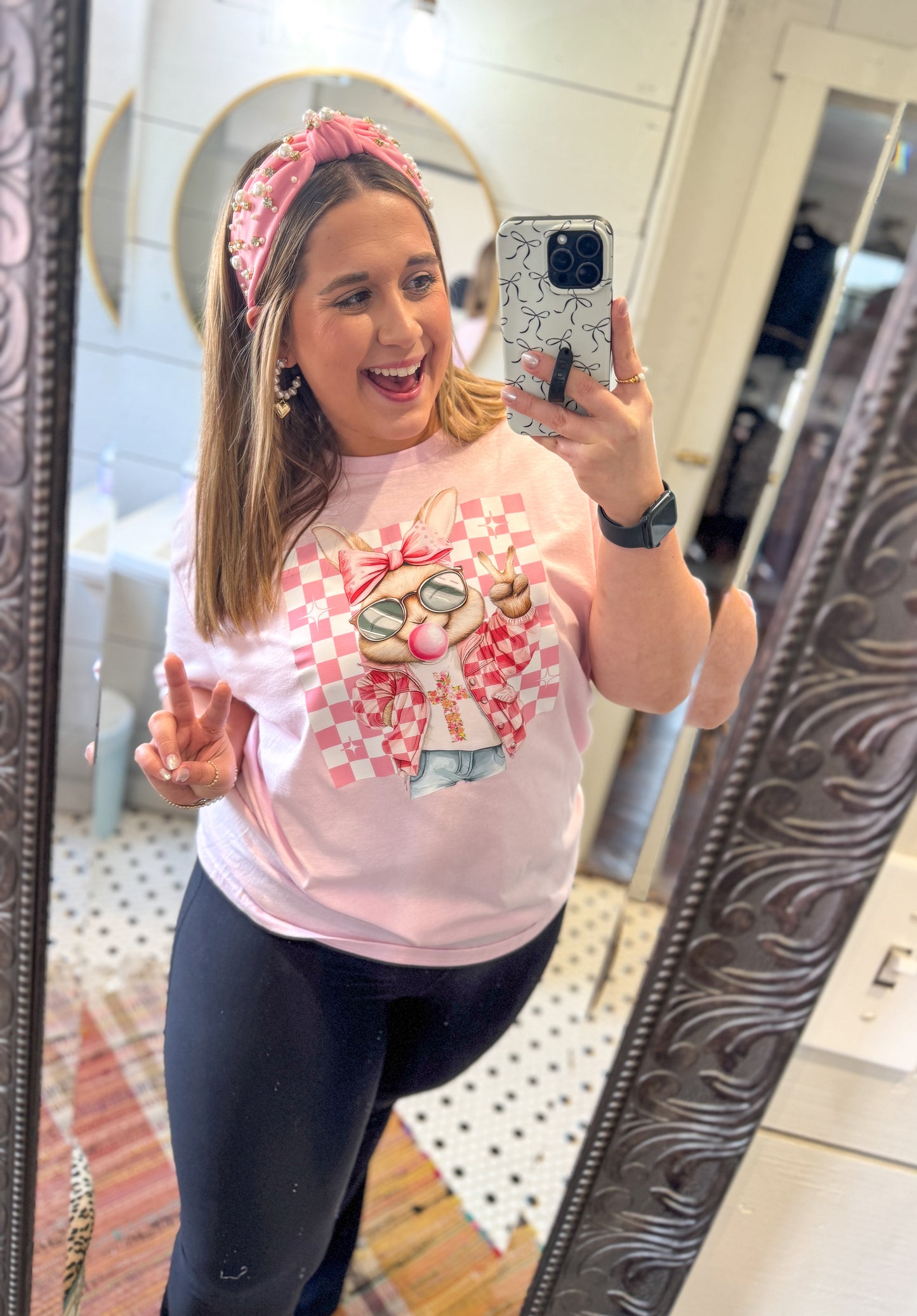 Person wearing a pink graphic t-shirt and dark leggings taking a mirror selfie.