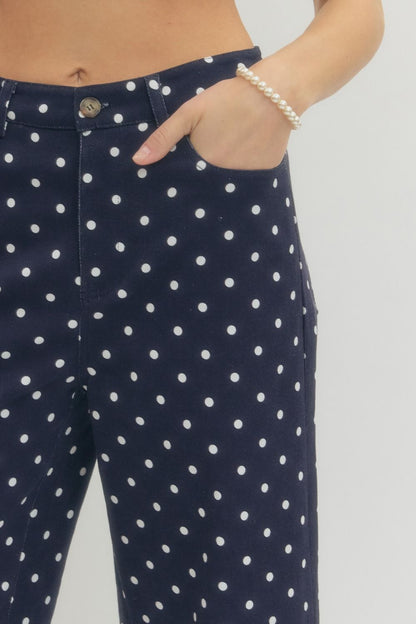 Navy blue pants with white polka dots worn by a person on a plain background