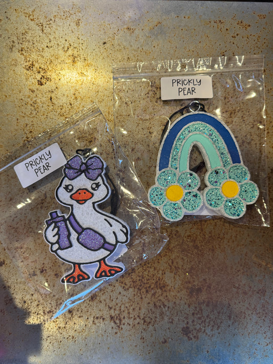 Two decorative pins in clear packaging on a rusty surface, with 'Prickly Pear' labels.