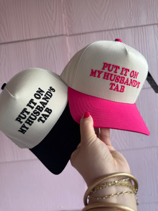 Two baseball caps with text held by a hand against a light pink background