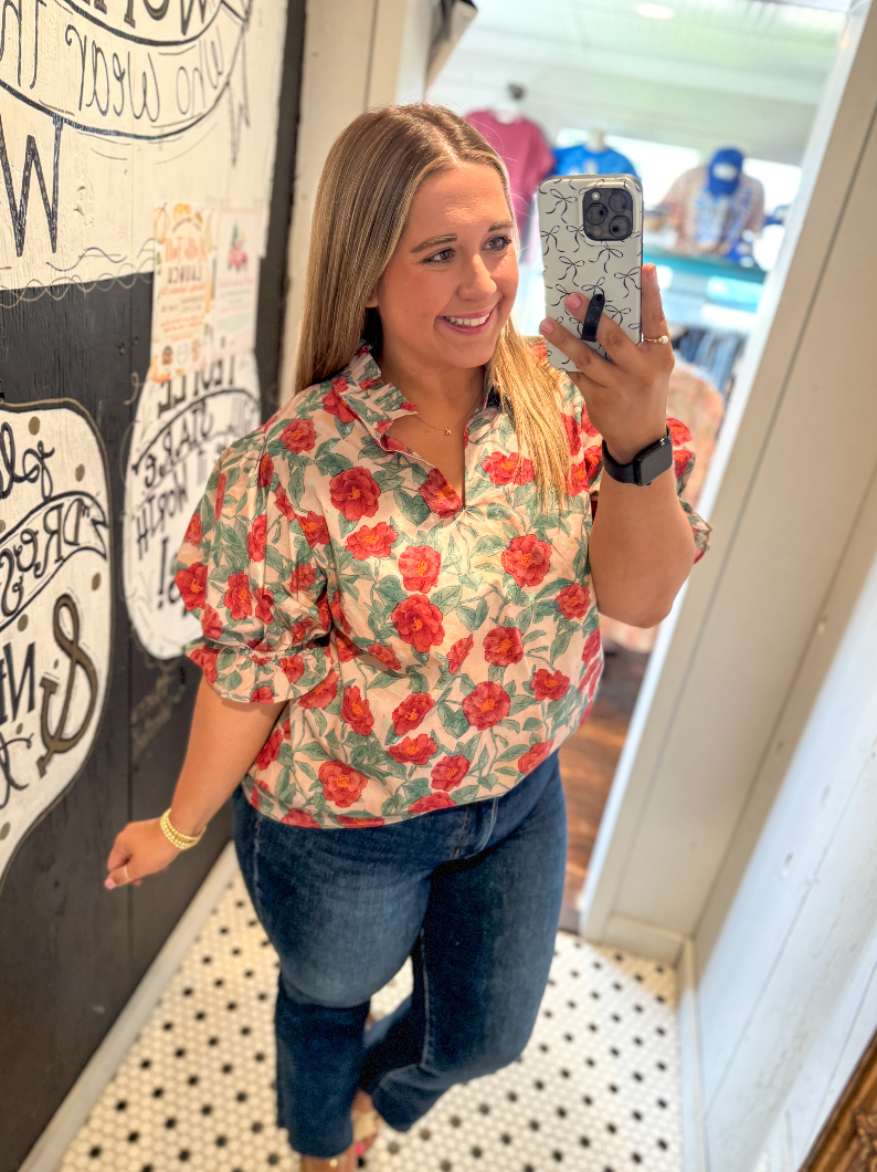 Woman taking a mirror selfie wearing a floral shirt and jeans in a casual setting.