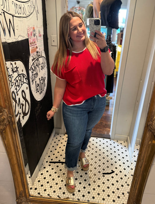 Woman taking a mirror selfie wearing a red top and blue jeans in a room with a decorative mirror.