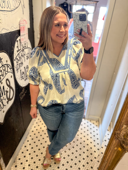 Woman taking a mirror selfie wearing a patterned top and jeans in a store.