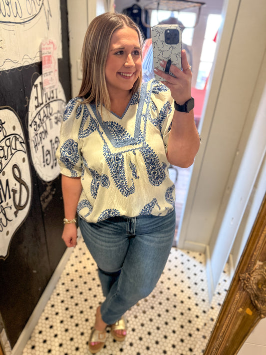 Woman taking a mirror selfie wearing a patterned top and jeans in a store.