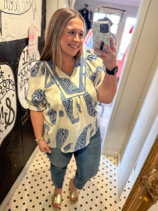 Woman taking a mirror selfie wearing a patterned top and jeans indoors.