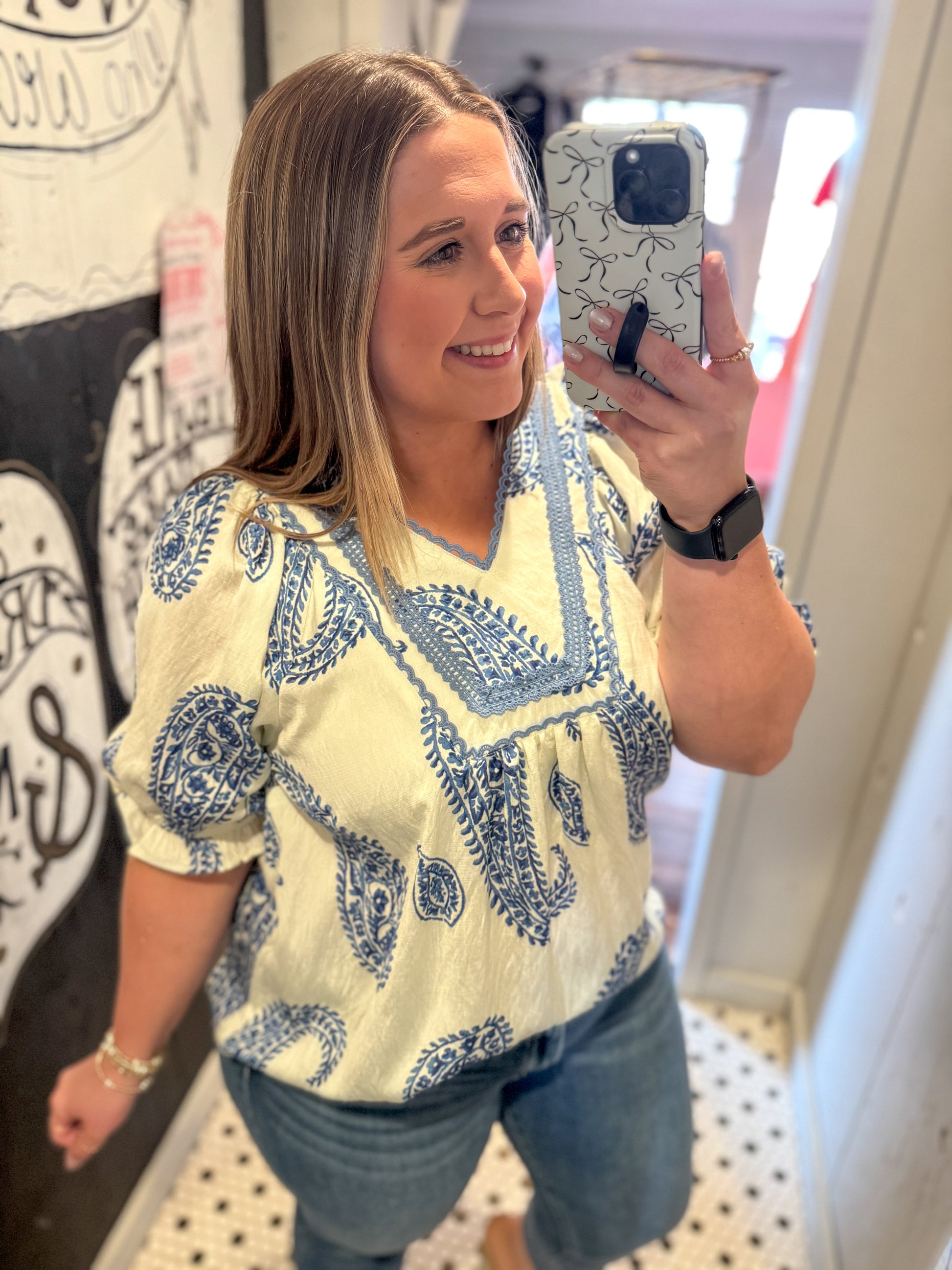 Woman taking a mirror selfie wearing a yellow and blue patterned top.