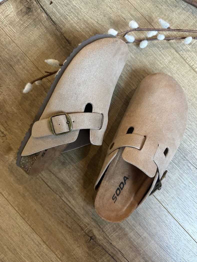 Pair of tan suede clogs with a buckle on a wooden floor.