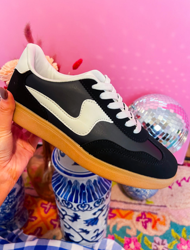 Black and white sneaker held in front of a colorful background with decorative elements.