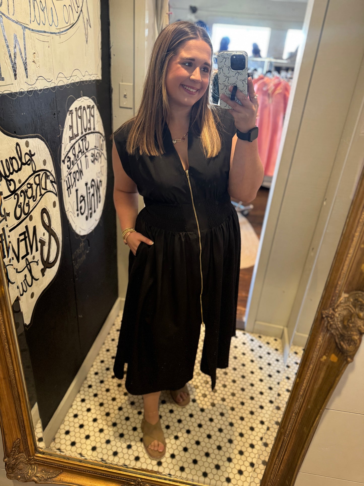 Woman taking a mirror selfie wearing a black dress in a store.