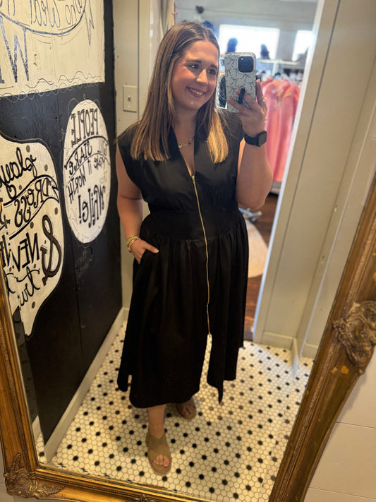Woman taking a mirror selfie wearing a black dress in a store.
